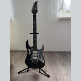 Černá elektrická kytara s ostře tvarovaným korpusem a hmatníkem zdobeným bílými ornamenty. Na hlavě je bílý nápis Zanez. Nástroj má dva humbuckery, j…