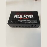 Černý napájecí zdroj pro efektové pedály s nápisy Voodoo Lab, PEDAL POWER 2 PLUS a tabulkou specifikací 9 VOLT ISOLATED DC OUTPUTS. Na přední straně…