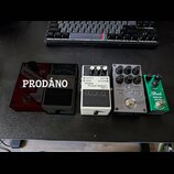 Pět efektových pedálů v řadě na černém povrchu. Zleva je červený pedál, černý pedál s nápisem boss a bílý pedál s nápisy Noise Suppressor NS-2 a boss…