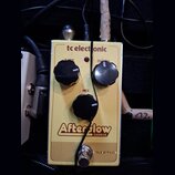 Žlutý efekt pedál s nápisy tc electronic, Afterglow a CHORUS. Na horní části jsou dva černé oválné knoflíky s popisky RATE a DEPTH, uprostřed je jede…