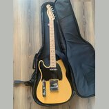 Žlutá elektrická kytara typu Telecaster s černým pickguardem a světle hnědým hmatníkem. Na hlavě je nápis Fender Squier. Kytara leží v černém polstro…
