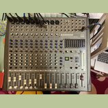 Šedý mixovací pult s nápisy SAMSON L1200 LIVE MIXING CONSOLE, 24 DSP a USB. Zařízení obsahuje řadu vstupních kanálů s potenciometry, přepínači a posu…
