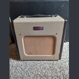 Kytarový kombo zesilovač s béžovým povrchem z texturovaného vinylu a tmavě hnědými hranami. Na přední straně je umístěn oválný fialový štítek s nápis…