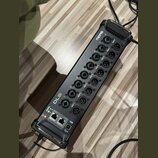 Černý digitální stagebox s kovovým šasi a madlymi po stranách. Na horní části je nápis Midas a řada konektorů XLR označených jako OUT 1 až OUT 8. V d…