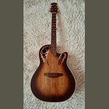 Akustická kytara s vyřezávanými otvory v horní desce místo klasického rozetového otvoru. Nástroj má tmavě hnědý přechodový povrch (sunburst) a hmatní…