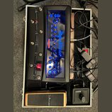 V hliníkovém kufru se nachází černý kytarový procesor s modře podsvíceným panelem a nápisem Hughes & Kettner Black Spirit 200. Zařízení obsahuje řadu…