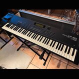 Černý digitální klavír Roland XP-80 Music Workstation na černém kovovém stojanu. Nástroj má standardní klávesnici a horní panel s displejem, tlačítky…