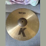 Zlatavý mosazný činel s viditelným kovánívým povrchem. Na horní části je černý nápis SWEET CRASH a pod ním menší text 19"/48 cm. Ve spodní části je v…