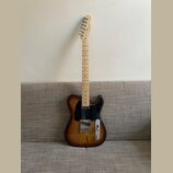 Elektrická kytara typu Telecaster s dřevem s výraznou žilnatostí a tmavě hnědým přechodem k okrajům. Nástroj má černý pickguard, jeden krkový snímač…