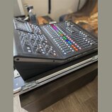 Černý digitální mixážní pult s displejem a množstvím posuvníků, knoflíků a barevných tlačítek. Na pravém předním okraku je bílý nápis MIDAS. Zařízení…