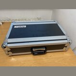 Černý transportní kufr s hliníkovými hranami a kovovými rohy. Na horní části je bílá nálepka s nápisy „FlyRig 30“ a „PORTABLE MULTI-EFFECT PROCESSOR“…