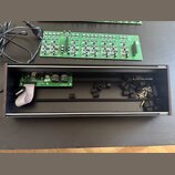 Fotografie zobrazuje dvě zelené elektronické desky s osazenými součástkami a černý obdélníkový šasi z tmavého dřeva. Na jedné z desek je vidět nápis…