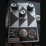 Kytarový efekt pedál s kovovým stříbrným povrchem a černými geometrickými prvky. Na horní části jsou tři černé oválové knoflíky s popisky DELAY, MIX…