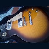 Elektrická kytara typu Les Paul s barevným přechodem od žluté k tmavě hnědé (sunburst). Nástroj má dva humbuckery s krémovými rámečky, chromovaný kob…