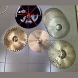 Sestet činelů v různých barvách a velikostech. Černý činel nese nápisy „Pitch Black“ a „Zildjian“. Jeden z mosazných činelů má nápisy „PAISTE“, „404“…