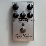Stříbrný efekt pedál s kovovým, třpytivým povrchem. Na horní části jsou čtyři černé otočné ovladače s nápisy OUTPUT, DISTORTION, BASS, MID a TREBLE.…