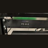 Černý rackový rozvodč rač s nápisy POWER BASE, PB 4x4 a POWER DISTRIBUTION SYSTEM. Zařízení je přišroubované do rackového stojanu pomocí čtyř šroubů.…