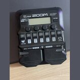 Černý multi-efektový procesor s nápisy G1 FOUR, ZOOM a Multi-Effects Processor. Zařízení obsahuje displej, čtyři ovládací knofíky s popisky Lo, Mid,…