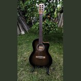 Akustická kytara s tmavě hnědým přechodovým povrchem (sunburst) a vyřezem v korpusu. Na hlavě hmatníku je nápis Carl a uvnitř ozvučnice je vidět štít…