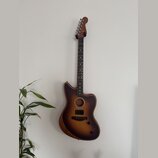 Akustická kytara s vyřezem v korpusu a tmavě hnědým přechodovým lakováním (sunburst). Na hlavě hmatníku je viditelné logo Fender. Nástroj visí na stě…