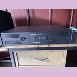 Černý výkonový zesilovač v kovovém šasi s nápisy AMERICAN AUDIO a PROFESSIONAL POWER AMPLIFIER. Na předním panelu je uprostřed označení modelu VLP150…