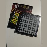 Černý MIDI kontrolér Novation Launchpad Mini s mřížkou bílých podsvícených políček. Na pravém okraji je svisle napsáno LAUNCHPAD MINI a v pravém doln…