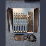 Modrý mixovací pult s nápisem YAMAHA a označením modelu MG12/4. Zařízení obsahuje několik kanálů s posuvníky, otočnými knoflíky a tlačítky v červené…