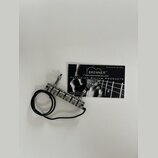 Kovový tremolo systém pro kytaru s černým přívodním kabelem. Vedle nástavce leží vizitka s nápisy BRENNER™, WWW.BRENNERUSA.COM, PRECISION GUITAR PROD…