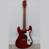 Elektrická kytara s červeným metalickým povrchem těla a hnědým hmatníkem. Na hlavě je bílý nápis "Cort". Kytara má bílý pickguard, jeden snímač typu…