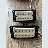 Dvě bílé humbucker snímače v černých plastových rámečkách s přiloženými barevnými vodiči. Na spodním snímači je vpravo vyryt nápis FISHMAN. Povrchy j…