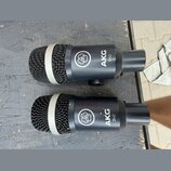 Dvě dynamická mikrofony černé barvy s kovovými mřížkami a šedým kroužkem v horní části. Na těle obou mikrofonů je bílé logo ve tvaru květiny a nápis…