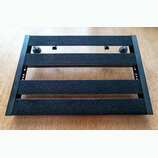 Černý obdélníkový pedalboard s třemi vodorovnými lištami potaženými černým hrubým povrchem. Boční rám je vyroben z černého materiálu s viditelnými ot…