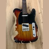 Elektrická kytara typu Telecaster s dřevem v přirozené barvě a tmavě hnědým, nepravidelným „spáleným“ vzorem. Má černý pickguard a jeden snímač u mos…
