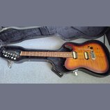 Elektrická kytara s trupem v přechodové barvě od žluté po tmavě hnědou, umístěná v černém tvrdém kufru. Nástroj má dva humbuckery a most s vibrační p…