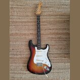 Elektrická kytara typu Stratocaster s barevným přechodem korpusu od černého přes červený k žlutému. Na hlavě hmatníku je viditelné logo Fender. Kytar…