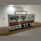Kytarový zesilovač značky Orange, model Tiny Terror, v bílém provedení s kovovou rukojetí. Na předním panelu je velký černý nápis ORANGE a menší text…
