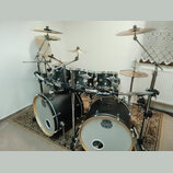 Černá bicí souprava s bílými لديmi a chromovaným kováním. Na basových bubnech je logo MAPEX, na tomarech jsou vidět loga Mapex a na nosném systému ná…