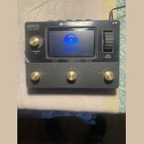 Černý loop pedal s kovovým povrchem a zlatými ovládacími prvky. Na zařízení jsou nápisy „AEROS Gold Edition“, „SINGULAR SOUND“ a na displeji text „AE…