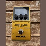 Zlatý efekt pedál s nápisy AMP CORE STUDIO a NUX. Horní část obsahuje displej, tři černé ovládací knoflíky a konektory USB, DC 9V a MIDI. Na spodní č…