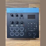 Černý trigger modul s modrým horním panelem. Na modré části je bílý nápis Roland TRIGGER MODULE TM-6 PRO. Zařízení obsahuje displej, několik otočných…