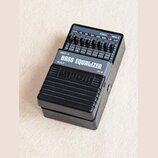 Černý kytarový pedál s nápisy MEQ-2 a BASS EQUALIZER. Zařízení obsahuje devět posuvníků s označením LEVEL, 40, 80, 150, 300, 600, 1.2K, 2.4K a kontro…