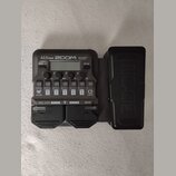 Černý multi-efektový procesor s nápisy A1X FOUR, ZOOM a Multi-Effects Processor. Zařízení obsahuje displej, několik ovládacích tlačítek s popisky jak…