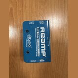 Modrý obdélníkový box s nápisy Radial engineering, PRO-RMP STUDIO REAMPER a TRANSFORMER ISOLATED PASSIVE REAMP. Na horní části je velký bílý nápis Re…