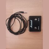 Černý spínací pedál s připojeným kabelem a jack konektorem. Na přední straně je bílé logo Marshall a dvě stříbrná tlačítka s nápisy Reverb a Channel.…