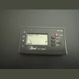 Černý digitální ladicí přístroj s LCD displejem. Na spodní straně je bílý nápis Blond ET-68C. Vpravo se nachází červené tlačítko ON/OFF a tři oválná…