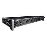Černý rackový audio rozhraní s kovovým šasi a stříbrnými bočními konzolami. Na předním panelu je nápis TASCAM US-20x20, přepínač STANDBY/ON a osm kom…
