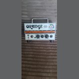 Bílý kytarový zesilovač s kovovou rukojetí a černými nohami. Na horním panelu je nápis ORANGE, MICRO TERROR a 20W RMS spolu s barevným logem. Ovládac…