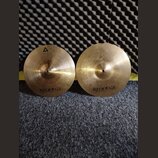 Dvě mosazné činely s viditelným opracováním povrchu. Oba mají v dolní části nápis istanbul Agop Made in Turkey. Levý činel má navíc v horní části tro…