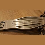 Detailní pohled na kovový pedál v stříbrné barvě s broušeným povrchem. Na horní části je vyryt nápis Speedcobra 310. Povrch vykazuje drobné škrábance…