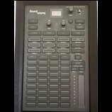 Šedý profesionální kontrolér osvětlení s nápisem Sound Switch a označením PROFESSIONAL LIGHTING CONTROLLER. Zařízení obsahuje mřížku tlačítek s popis…